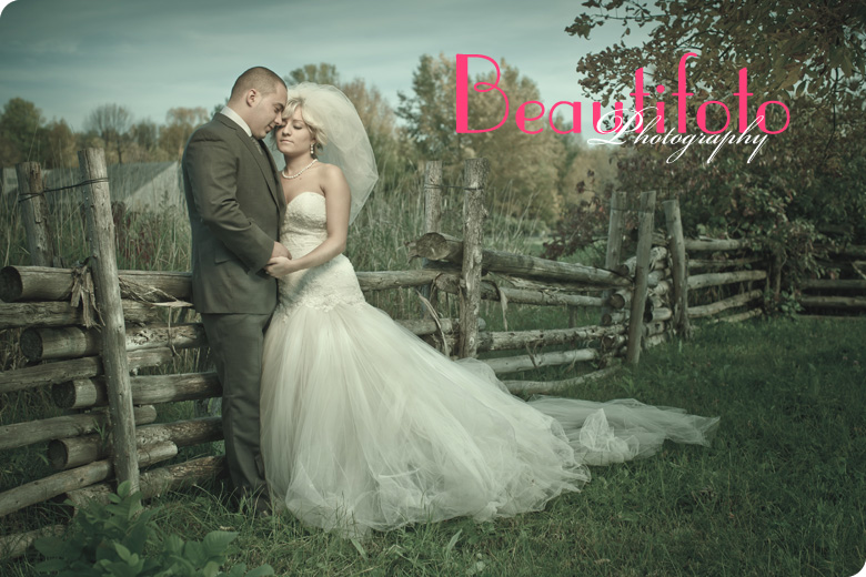 Bride and groom embrace by an old wooden fence.