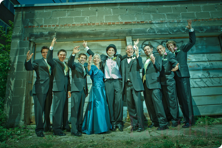 the groom and his parents with the ushers posing by an old garage door
