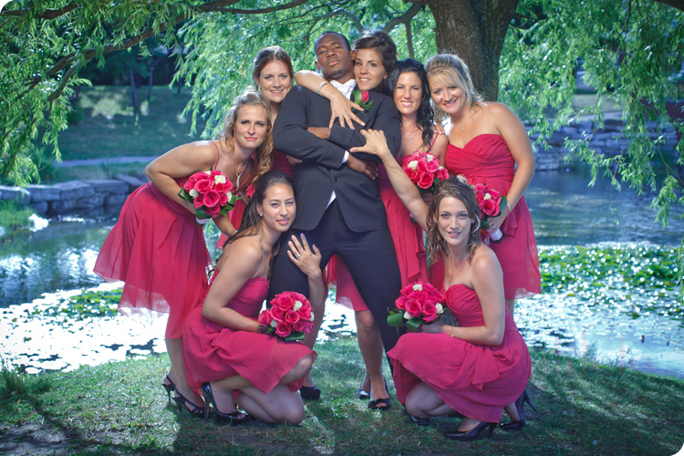 the groom poses with the bridemaids with pink dresses in the park 