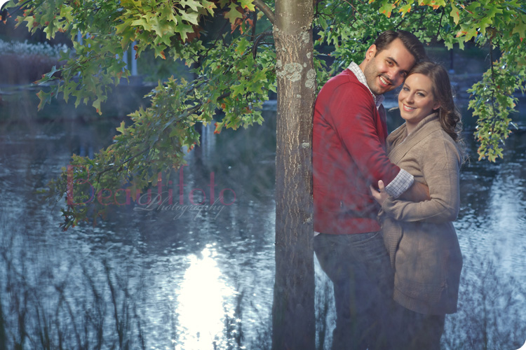 a couple embracing by a tree next to a lake