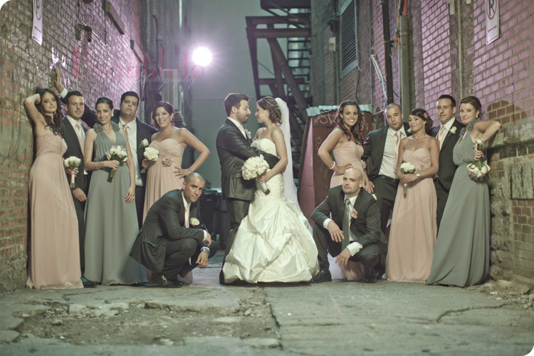 The bride and groom and the bridal party posing in an alley 